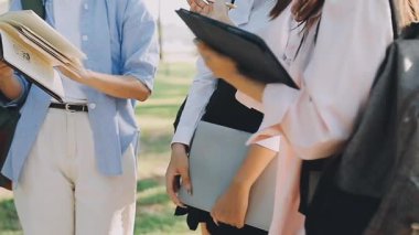 Asyalı genç kız öğrenci elinde kitap tutuyor ve parktaki üniversite binasının yanında dikilirken gözlerini kaçırıyor.