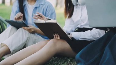 Genç Asyalı kız öğrenci bahçede ders çalışıyor ve kitap okuyor.