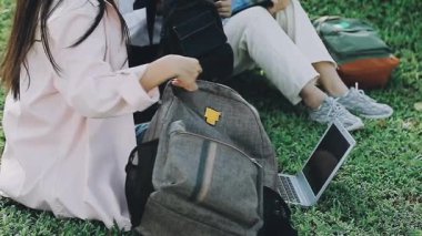 Genç Asyalı kadın dizüstü bilgisayar kullanıyor ve parkta kitap okuyor.