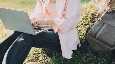 Parkta dizüstü bilgisayar kullanan genç bir kadın..