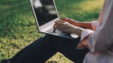 Şehirdeki yeşil çimlerin üzerinde dizüstü bilgisayarla çalışan bir kadın..