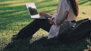 Parkta dizüstü bilgisayar kullanan genç bir kadın.