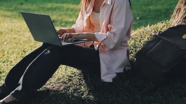 Parktaki yeşil çimlerde oturan dizüstü bilgisayar kullanan bir kadın..