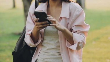 Sonbahar parkında elinde cep telefonu olan beyaz tişörtlü genç bir kadın.