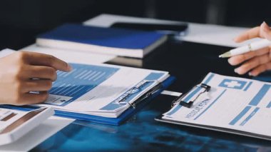 Kadın eli mavi takımlı, elinde kalem ve belgeler var.