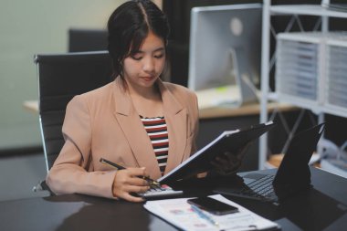 Telework konsepti - Asyalı iş kadını video toplantısına katılmak için dizüstü bilgisayar kullanır ve evdeki dijital tabletine notlar yazar