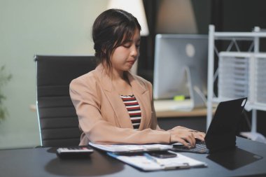 Telework konsepti - Asyalı iş kadını video toplantısına katılmak için dizüstü bilgisayar kullanır ve evdeki dijital tabletine notlar yazar