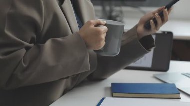 Akıllı telefon kullanan ve ofiste dizüstü bilgisayarda çalışan bir iş adamı.