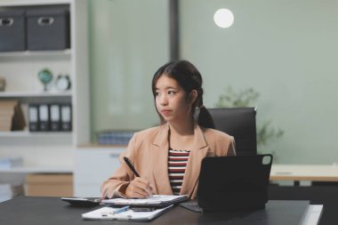 Telework konsepti - Asyalı iş kadını video toplantısına katılmak için dizüstü bilgisayar kullanır ve evdeki dijital tabletine notlar yazar