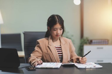 Telework konsepti - Asyalı iş kadını video toplantısına katılmak için dizüstü bilgisayar kullanır ve evdeki dijital tabletine notlar yazar