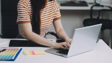 Gündelik giyinen genç bir kadın bilgisayarda çalışıyor ve evde evrak işleriyle uğraşıyor.