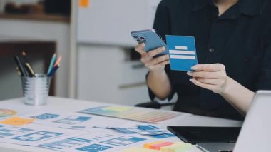 Günlük kıyafet giyen genç bir kadın dizüstü bilgisayarda çalışıyor, cep telefonunu internet üzerinden iş yapmak için kullanıyor..