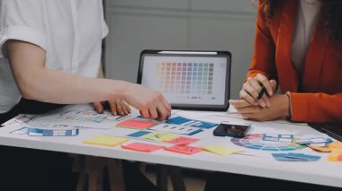 Genç yaratıcı tasarımcı dizüstü bilgisayarla masada oturuyor ve yeni projeyi tartışıyor.