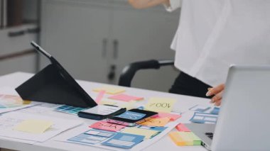 Dizüstü bilgisayarda çalışan ve yaratıcı ofisteki masada otururken cep telefonuyla konuşan sıradan giyinmiş genç bir kadın.