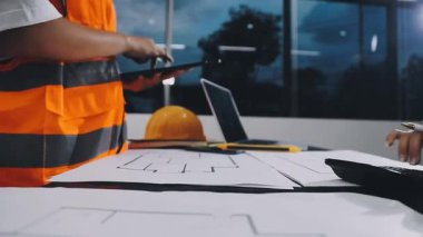 Ofiste çalışan miğferi, miğferi ve planı olan inşaat mühendisi.