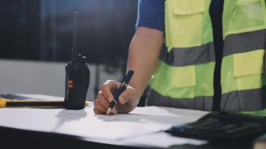 İnşaat alanında kalemle tablet kullanan bir adam. Mühendis, ofisteki planla çalışıyor.