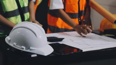 Miğferli ve güvenlik gözlüklü genç mimar inşaat masasının planlarıyla çalışıyor..