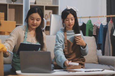 Genç Asyalı kadınlar müşterilerden gelen yeni siparişten sonra mutlu olurlar. Asyalı bir kadının online mağazasının satışındaki başarısının sürpriz ve şok edici yüzü. Çevrimiçi satış. Çevrimiçi Alışveriş