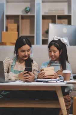 Genç Asyalı kadınlar müşterilerden gelen yeni siparişten sonra mutlu olurlar. Asyalı bir kadının online mağazasının satışındaki başarısının sürpriz ve şok edici yüzü. Çevrimiçi satış. Çevrimiçi Alışveriş