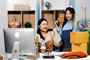 Genç Asyalı kadınlar müşterilerden gelen yeni siparişten sonra mutlu olurlar. Asyalı bir kadının online mağazasının satışındaki başarısının sürpriz ve şok edici yüzü. Çevrimiçi satış. Çevrimiçi Alışveriş