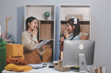 Genç Asyalı kadınlar müşterilerden gelen yeni siparişten sonra mutlu olurlar. Asyalı bir kadının online mağazasının satışındaki başarısının sürpriz ve şok edici yüzü. Çevrimiçi satış. Çevrimiçi Alışveriş