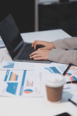 Hesap makinesi ve yazı kullanan bir iş kadını, hesap makinesiyle not alır. Ofiste çalışan bir kadın. Masasında dizüstü bilgisayar ve belgeler var.