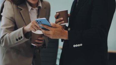 Genç işadamları kupa tutuyorlar ve ofiste konuşuyorlar.