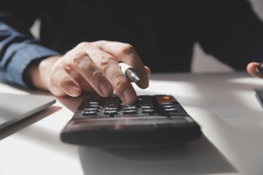 İş adamı masabaşında hesap makinesi kullanarak rakamları hesaplıyor ve muhasebe kavramını finanse ediyor.