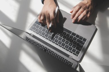Bir kahve dükkanında dizüstü bilgisayarı üzerinde çalışan genç bir adamın kırpılmış görüntüsü, iş adamının elleri ofis masasında dizüstü bilgisayarla meşgul, genç bir erkek öğrenci ahşap masada oturuyor.