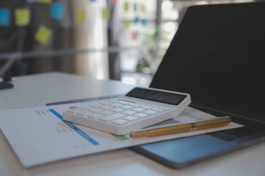 Close up view of simple workspace with laptop, notebooks, coffee cup and tree pot on white table with blurred office room background