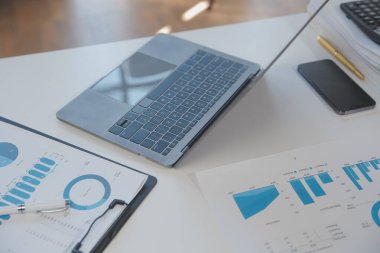 Close up view of simple workspace with laptop, notebooks, coffee cup and tree pot on white table with blurred office room background