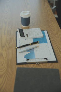 Close up view of simple workspace with laptop, notebooks, coffee cup and tree pot on white table with blurred office room background