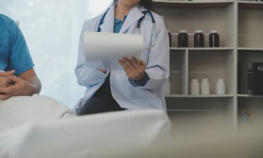 Genç doktor steteskop kullanıyor. Hastanın kalp atışlarını dinle. Kadın bir doktorun erkek bir hastaya muayene yaparken görüntüsü.