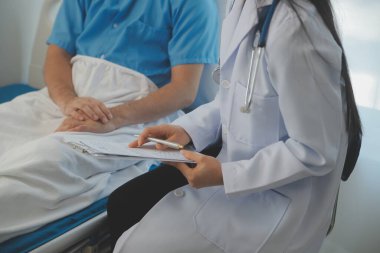 Genç doktor steteskop kullanıyor. Hastanın kalp atışlarını dinle. Kadın bir doktorun erkek bir hastaya muayene yaparken görüntüsü.