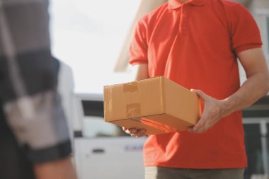 Asya teslimat ekspresi kuryesi genç adam, kadın müşteriye kutu veriyor. Evin önünde koruyucu yüz maskesi takıyor.