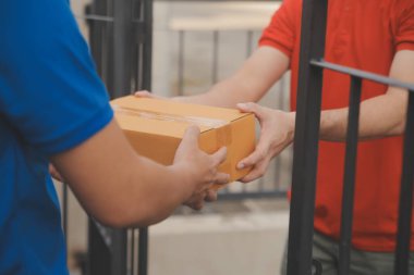 Asya teslimat ekspresi kuryesi genç adam, kadın müşteriye kutu veriyor. Evin önünde koruyucu yüz maskesi takıyor.
