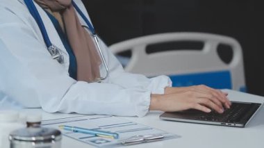 Ofisteki iş yerinde oturan ve dizüstü bilgisayar kullanan üniformalı genç bir doktor..