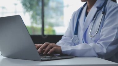 Masasında dizüstü bilgisayarı olan genç bir erkek doktor oturuyor..