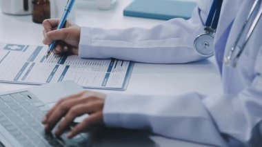 Kadın doktor dizüstü bilgisayar kullanıyor ve ofisteki bir tablete yazı yazıyor.