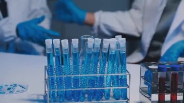 Mavi takım elbiseli bir bilim adamı elinde sıvı test tüpleri tutuyor.