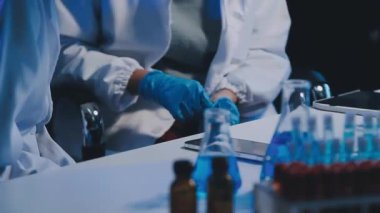 Yakın plan - koruyucu üniformalı ve koruyucu eldivenli bir laboratuvar çalışanı tüpü ve tüpü elinde tutuyor.