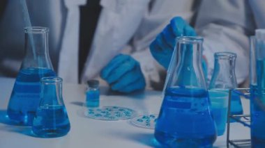 Laboratuvar asistanı elinde kimyasal çözeltiyle mavi tüp tutuyor..
