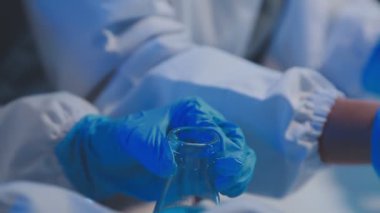 Koruyucu eldivenli bir laboratuar çalışanı çözeltisi olan bir sıvıyla bir bardak tutuyor.