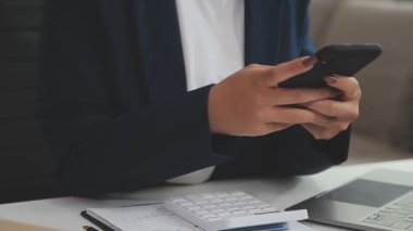 Ofiste çalışırken akıllı telefon kullanan genç bir kadın..