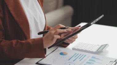 İş kadını ofisinde elinde kalem ve hesap makinesiyle tablet bilgisayar kullanıyor.