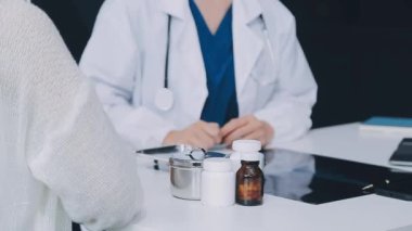 Kadın doktorun elinde steteskop ve arka planda bir hasta var..