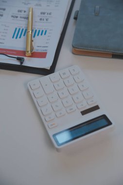 Close up view of simple workspace with laptop, notebooks, coffee cup and tree pot on white table with blurred office room background