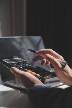 İş adamı masabaşında hesap makinesi kullanarak rakamları hesaplıyor ve muhasebe kavramını finanse ediyor.