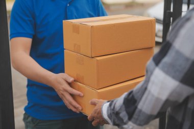 Asya teslimat ekspresi kuryesi genç adam, kadın müşteriye kutu veriyor. Evin önünde koruyucu yüz maskesi takıyor.