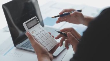 Modern ofisteki masanın üstünde dizüstü bilgisayar ve hesap makinesi kullanan iş adamları var..